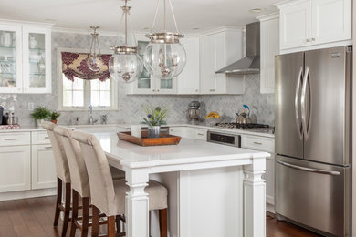 Example of a large transitional l-shaped bamboo floor and brown floor kitchen design in Other with a farmhouse sink, recessed-panel cabinets, white cabinets, granite countertops, gray backsplash, marble backsplash, stainless steel appliances, an island and white countertops
