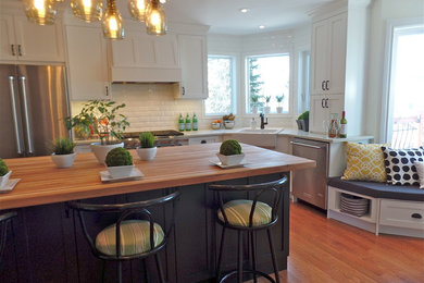 Large transitional u-shaped dark wood floor open concept kitchen photo in Calgary with a farmhouse sink, shaker cabinets, white cabinets, wood countertops, white backsplash, subway tile backsplash, stainless steel appliances and an island