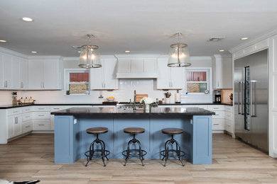 Large country l-shaped medium tone wood floor and brown floor eat-in kitchen photo in Houston with a farmhouse sink, shaker cabinets, white cabinets, solid surface countertops, white backsplash, subway tile backsplash, stainless steel appliances and an island