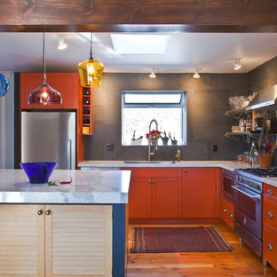 Idee per una cucina a L eclettica con elettrodomestici in acciaio inossidabile, ante arancioni, paraspruzzi grigio, paraspruzzi con piastrelle in pietra e ante con riquadro incassato