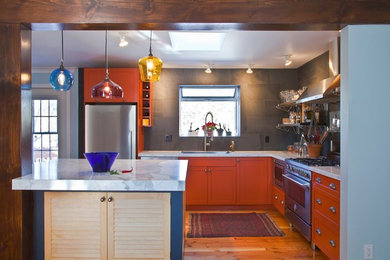 Cette image montre une cuisine bohème en L avec un électroménager en acier inoxydable, des portes de placard oranges, une crédence grise, une crédence en carrelage de pierre et un placard avec porte à panneau encastré.