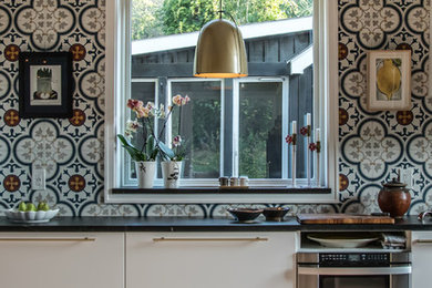 Bild på ett mellanstort lantligt kök, med en undermonterad diskho, släta luckor, vita skåp, bänkskiva i täljsten, flerfärgad stänkskydd, stänkskydd i cementkakel, rostfria vitvaror, tegelgolv och rött golv