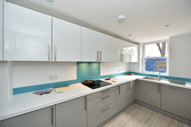 Photo of a medium sized modern u-shaped enclosed kitchen in Kent with a built-in sink, flat-panel cabinets, white cabinets, laminate countertops, blue splashback, glass sheet splashback, stainless steel appliances, ceramic flooring and no island.