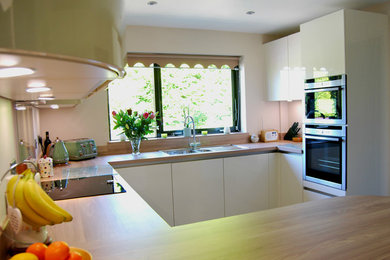 Small contemporary u-shaped kitchen/diner in Cheshire with flat-panel cabinets, white cabinets, laminate countertops, grey splashback, glass sheet splashback and a breakfast bar.
