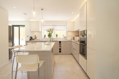This is an example of a medium sized contemporary l-shaped open plan kitchen in Sussex with a double-bowl sink, flat-panel cabinets, grey cabinets, quartz worktops, brown splashback, glass sheet splashback, stainless steel appliances, porcelain flooring, an island and beige floors.