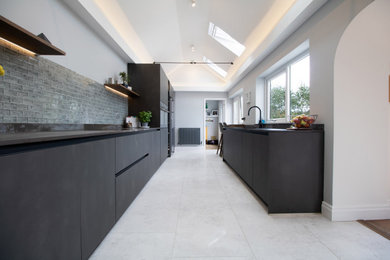 Photo of a medium sized modern galley enclosed kitchen in Cardiff with an integrated sink, flat-panel cabinets, black cabinets, engineered stone countertops, blue splashback, glass tiled splashback, black appliances, porcelain flooring, no island, white floors and multicoloured worktops.