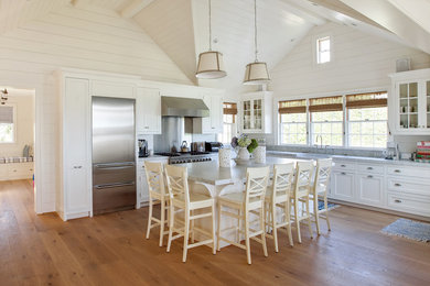 Inspiration for a large coastal l-shaped medium tone wood floor open concept kitchen remodel in Boston with a farmhouse sink, recessed-panel cabinets, white cabinets, marble countertops, gray backsplash, stainless steel appliances and an island