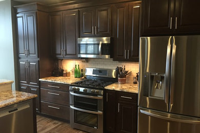 Example of a mid-sized classic medium tone wood floor open concept kitchen design in Other with raised-panel cabinets, dark wood cabinets, granite countertops, white backsplash, stone tile backsplash, stainless steel appliances and an island