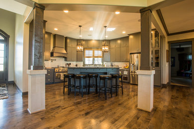 Large elegant l-shaped medium tone wood floor and brown floor open concept kitchen photo in Other with a double-bowl sink, shaker cabinets, gray cabinets, white backsplash, stainless steel appliances and an island