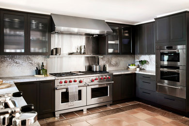 Aménagement d'une cuisine classique en U avec un placard à porte shaker, des portes de placard noires, un électroménager en acier inoxydable, une péninsule, un sol marron et un plan de travail gris.