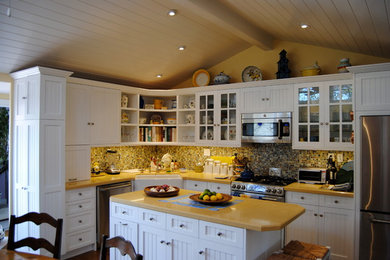 Eat-in kitchen - large traditional l-shaped dark wood floor eat-in kitchen idea in Orange County with a farmhouse sink, shaker cabinets, white cabinets, solid surface countertops, multicolored backsplash, mosaic tile backsplash, stainless steel appliances and an island