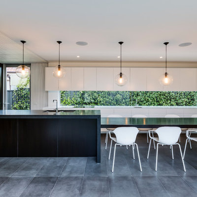 Example of a trendy galley ceramic tile and black floor eat-in kitchen design in Sydney with an undermount sink, flat-panel cabinets, wood countertops, an island, glass sheet backsplash and stainless steel appliances