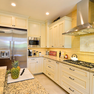 Photo of an expansive traditional u-shaped open plan kitchen in San Diego with a farmhouse sink, raised-panel cabinets, beige cabinets, granite benchtops, yellow splashback, ceramic splashback, stainless steel appliances, porcelain floors and with island.