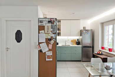 Mittelgroße Moderne Wohnküche ohne Insel in L-Form mit integriertem Waschbecken, grünen Schränken, Küchenrückwand in Weiß, Rückwand aus Keramikfliesen, Küchengeräten aus Edelstahl, Keramikboden und grauem Boden in Berlin