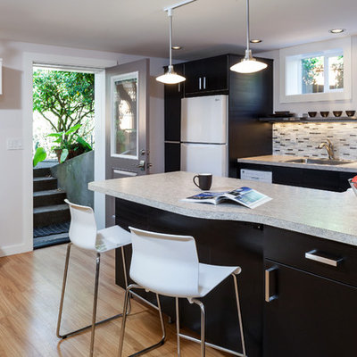 Eat-in kitchen - mid-sized contemporary u-shaped light wood floor and beige floor eat-in kitchen idea in Portland with a single-bowl sink, flat-panel cabinets, dark wood cabinets, solid surface countertops, multicolored backsplash, glass tile backsplash, white appliances and a peninsula