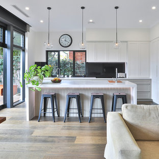This is an example of a large contemporary l-shaped open plan kitchen in Sydney with an undermount sink, shaker cabinets, white cabinets, quartz benchtops, black splashback, marble splashback, stainless steel appliances, medium hardwood floors, with island, brown floor and multi-coloured benchtop.