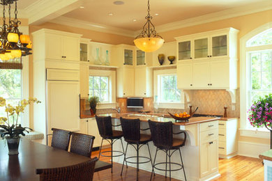 Example of a mid-sized classic l-shaped light wood floor, brown floor and coffered ceiling eat-in kitchen design in Charleston with an undermount sink, glass-front cabinets, white cabinets, brown backsplash, ceramic backsplash, white appliances, an island and brown countertops