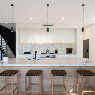 Inspiration for a contemporary l-shaped kitchen in Other with white cabinets, marble benchtops, marble splashback, stainless steel appliances, laminate floors, with island, an undermount sink, flat-panel cabinets, white splashback, brown floor and white benchtop.