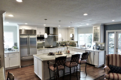 Example of a large transitional u-shaped medium tone wood floor and brown floor open concept kitchen design in Los Angeles with an undermount sink, recessed-panel cabinets, white cabinets, quartzite countertops, green backsplash, glass tile backsplash, stainless steel appliances, an island and multicolored countertops