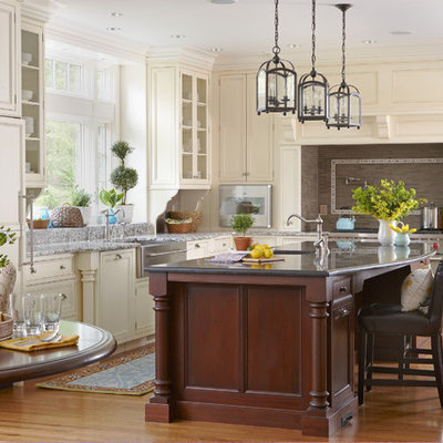 Inspiration for a large timeless l-shaped medium tone wood floor and brown floor eat-in kitchen remodel in Boston with recessed-panel cabinets, white cabinets, paneled appliances, a farmhouse sink, marble countertops, brown backsplash, mosaic tile backsplash and an island