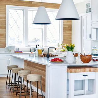 Photo of a beach style kitchen in New York with shaker cabinets, white cabinets, timber splashback, stainless steel appliances, white benchtop, beige splashback, light hardwood floors, multiple islands, beige floor and marble benchtops.