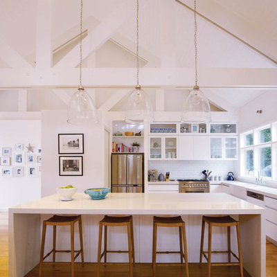 Example of a large beach style l-shaped medium tone wood floor open concept kitchen design in Melbourne with flat-panel cabinets, white cabinets, white backsplash, subway tile backsplash, stainless steel appliances and an island