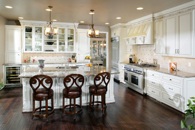 Inspiration for a large timeless l-shaped dark wood floor and brown floor enclosed kitchen remodel in Sacramento with an undermount sink, raised-panel cabinets, white cabinets, granite countertops, beige backsplash, stone tile backsplash, stainless steel appliances and an island