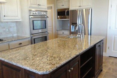 Large transitional u-shaped ceramic tile enclosed kitchen photo in Austin with an undermount sink, raised-panel cabinets, white cabinets, granite countertops, beige backsplash, stone tile backsplash, stainless steel appliances and an island