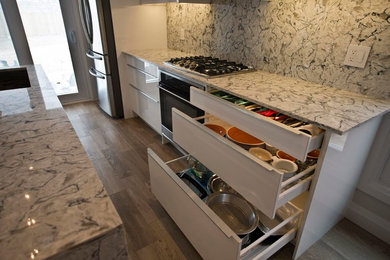 Eat-in kitchen - mid-sized modern medium tone wood floor eat-in kitchen idea in Toronto with an undermount sink, flat-panel cabinets, white cabinets, quartz countertops, stone slab backsplash and stainless steel appliances