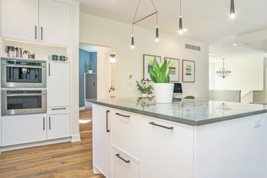 Photo of a large traditional l-shaped kitchen/diner in Grand Rapids with shaker cabinets, white cabinets, engineered stone countertops, stainless steel appliances, an island, grey worktops, a submerged sink, white splashback, ceramic splashback, medium hardwood flooring and brown floors.