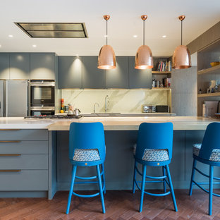 Inspiration for a contemporary galley open plan kitchen in London with flat-panel cabinets, blue cabinets, white splashback, black appliances, dark hardwood flooring, a breakfast bar, brown floors and white worktops.