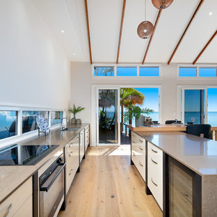 Design ideas for a beach style galley kitchen in Brisbane with an undermount sink, flat-panel cabinets, white cabinets, light hardwood floors, with island, beige floor and window splashback.