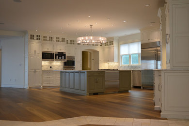 Example of a large transitional u-shaped medium tone wood floor eat-in kitchen design in Providence with raised-panel cabinets, white cabinets, granite countertops, white backsplash, stone tile backsplash, stainless steel appliances, an island and an undermount sink