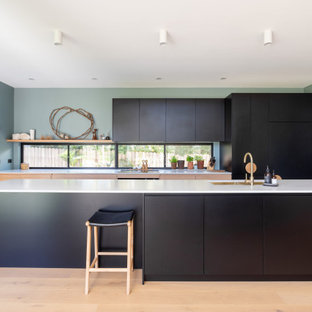 Inspiration for a contemporary galley kitchen in Wollongong with an undermount sink, flat-panel cabinets, black cabinets, panelled appliances, light hardwood floors, with island, beige floor and white benchtop.