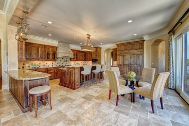 Large tuscan u-shaped travertine floor and beige floor eat-in kitchen photo in Austin with an undermount sink, raised-panel cabinets, medium tone wood cabinets, granite countertops, beige backsplash, ceramic backsplash, paneled appliances and an island