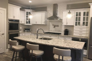Eat-in kitchen - mid-sized transitional l-shaped brown floor eat-in kitchen idea in Providence with an undermount sink, white cabinets, granite countertops, white backsplash, subway tile backsplash, stainless steel appliances, an island, recessed-panel cabinets and multicolored countertops