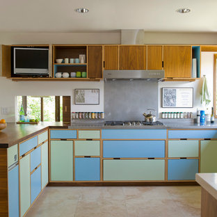 Modelo de cocina minimalista con encimera de acero inoxidable, electrodomésticos de acero inoxidable, armarios con paneles lisos, puertas de armario azules, salpicadero metalizado y salpicadero de metal