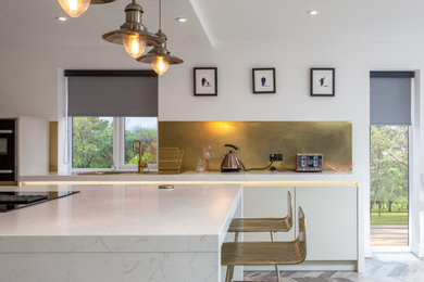 Photo of a large contemporary open plan kitchen in Manchester with an integrated sink, flat-panel cabinets, beige cabinets, marble worktops, metallic splashback, metal splashback, stainless steel appliances, porcelain flooring, an island, multi-coloured floors and white worktops.