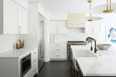 This is an example of a contemporary l-shaped kitchen in Philadelphia with a belfast sink, shaker cabinets, white cabinets, white splashback, stone slab splashback, stainless steel appliances, dark hardwood flooring, an island, brown floors and white worktops.