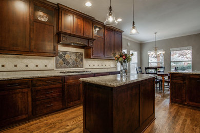 Example of a mid-sized classic u-shaped medium tone wood floor kitchen pantry design in Dallas with shaker cabinets, dark wood cabinets, granite countertops, beige backsplash, stone tile backsplash, stainless steel appliances and an island