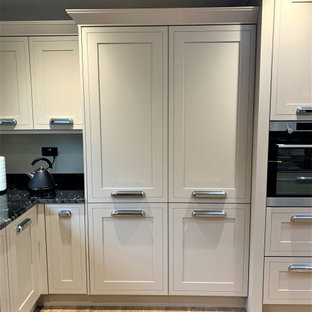 Photo of a large traditional u-shaped open plan kitchen in Other with a double-bowl sink, shaker cabinets, medium wood cabinets, granite benchtops, black splashback, black appliances, vinyl floors, with island and black benchtop.