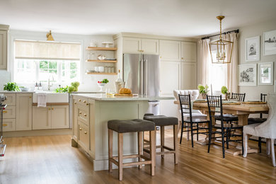 Eat-in kitchen - mid-sized transitional l-shaped brown floor and medium tone wood floor eat-in kitchen idea in Boston with a farmhouse sink, shaker cabinets, beige cabinets, marble countertops, white backsplash, subway tile backsplash, stainless steel appliances, an island and white countertops