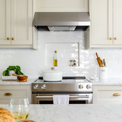 Eat-in kitchen - mid-sized transitional l-shaped light wood floor and brown floor eat-in kitchen idea in Boston with a farmhouse sink, shaker cabinets, beige cabinets, marble countertops, white backsplash, subway tile backsplash, stainless steel appliances, an island and white countertops