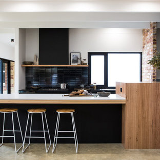 Inspiration for an expansive contemporary galley kitchen in Other with solid surface benchtops, black splashback, concrete floors, grey floor, white benchtop, black cabinets and a peninsula.