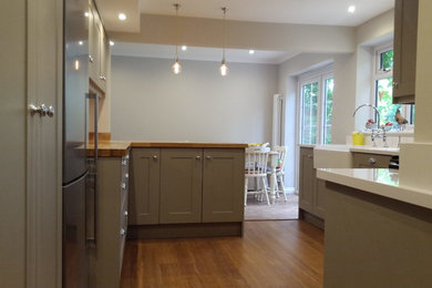 Inspiration for a medium sized traditional galley open plan kitchen in Surrey with a belfast sink, shaker cabinets, brown cabinets, wood worktops, multi-coloured splashback, mosaic tiled splashback, stainless steel appliances, light hardwood flooring and a breakfast bar.