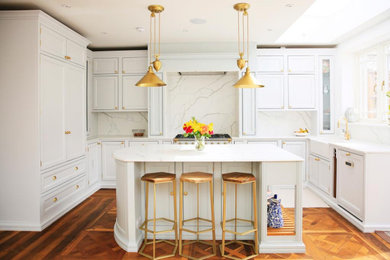 Example of a transitional u-shaped medium tone wood floor kitchen design in London with a farmhouse sink, recessed-panel cabinets, white cabinets, white backsplash, stone slab backsplash, an island and white countertops