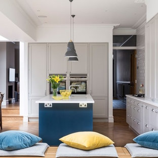 Inspiration for a medium sized traditional galley kitchen/diner in London with shaker cabinets, blue cabinets, medium hardwood flooring, an island, brown floors, a submerged sink and stainless steel appliances.