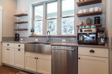 Example of a transitional u-shaped enclosed kitchen design in Portland with a farmhouse sink, shaker cabinets, white cabinets, wood countertops, gray backsplash, stainless steel appliances and an island