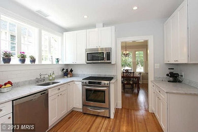 Example of a small transitional u-shaped dark wood floor enclosed kitchen design in DC Metro with an undermount sink, shaker cabinets, white cabinets, marble countertops, white backsplash, ceramic backsplash, stainless steel appliances and no island