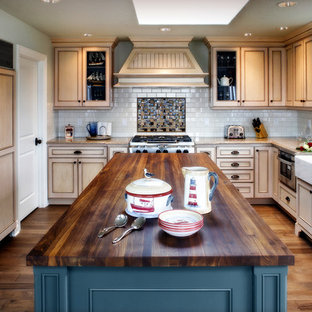 Design ideas for a mid-sized beach style u-shaped separate kitchen in Portland with a farmhouse sink, recessed-panel cabinets, beige cabinets, wood benchtops, white splashback, subway tile splashback, panelled appliances, medium hardwood floors and with island.